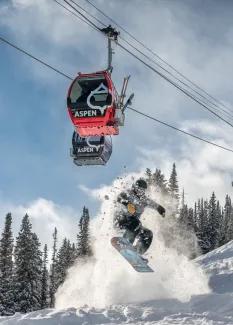 snowboarder jumping at aspen mountain under the gondola